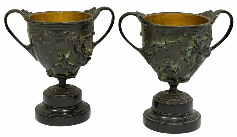 (2) Bronze Kantharos Chalices, Grand Tour Souvenir Glasses: (2) Bronze Kantharos Chalices, Grand Tour Souvenir Glasses. These unique chalices features intricate relief figures depicting mythological scenes. They appear to be mounted on a circular base. They