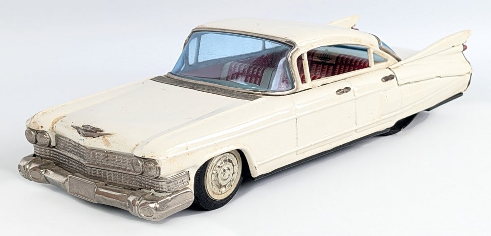 Bandai Tin Friction Cadillac: Banda tin friction Cadillac. The car has scratches and wear from play and age. It is missing the driver side rear hubcap. Measures approximately 11" long.