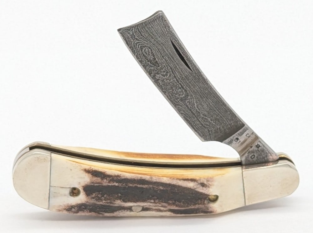 Case XX Stag Damascus Razor Knife: Knife has a purposeful grind mark across the tang like it was a factory reject. Knife is in nice condition with light scuffs and tarnishing on the bolsters, and a pin crack on the front handle scale. 