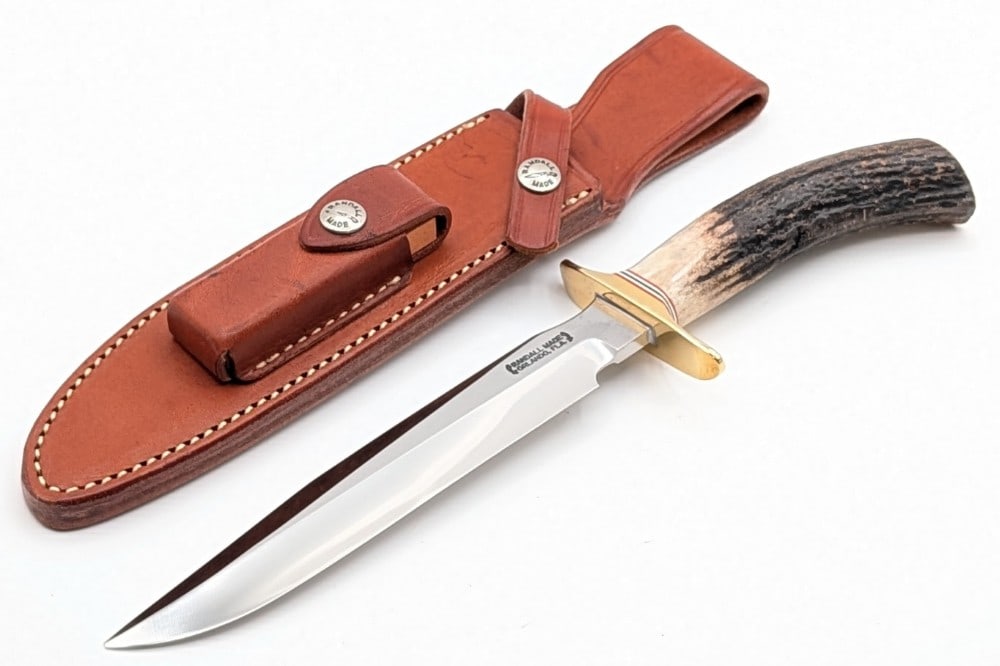 Randall Model 1 7in Stag All Purpose Fighter w/ Sheath: Features a brass double downturned guard, and a stag handle. Knife is in very nice condition with the very tip sadly broken off, and light scuffs and tarnishing on the guard from handling. Blade lengt