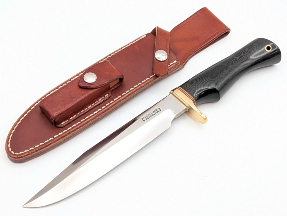 1980's Randall Model 1 7in All Purpose Fighter w/ Sheath: Features thumb notches on the spine, a brass single downturned guard, and a black micarta single finger groove handle with a lanyard hole. Knife is in like new condition. Blade length measures