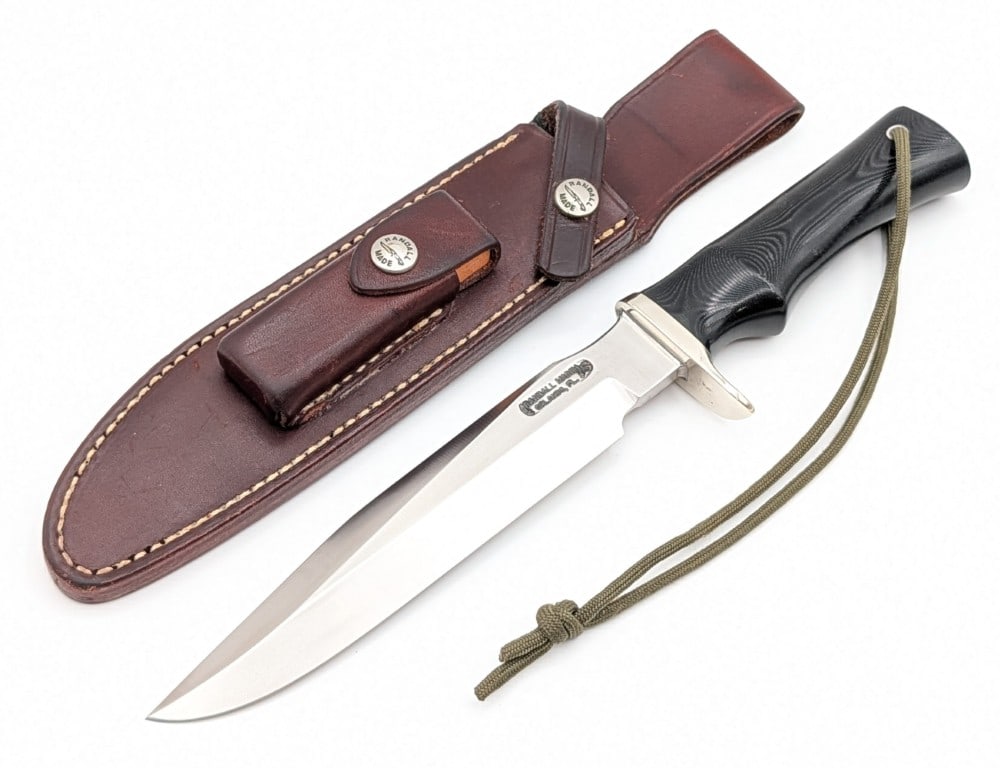 Randall Model 1 7in All Purpose Fighter w/ Sheath: Features a stainless steel blade, a nickel silver single downturned guard, a full tang handle construction, and a black micarta single finger groove handle with a lanyard hole. Knife is in nice condit