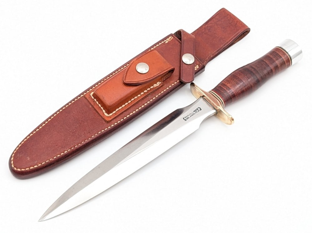1970's Randall Model 2 8in Fighting Stiletto w/ Rough Back Sheath: Features a brass double downturned guard, a stacked leather handle, a duralumin butt cap, and a nut pommel. Knife is in nice aged condition with light scratches and tarnishing on the polished blade, a