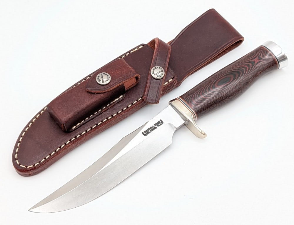 Randall Model 12 6in Little Bear Bowie w/ Sheath: Features thumb notches on the blade, a nickel silver single downturned guard, a micarta handle, and a duralumin butt cap. Knife is in like new condition. Blade length measures 6in and overall 10-3/4in