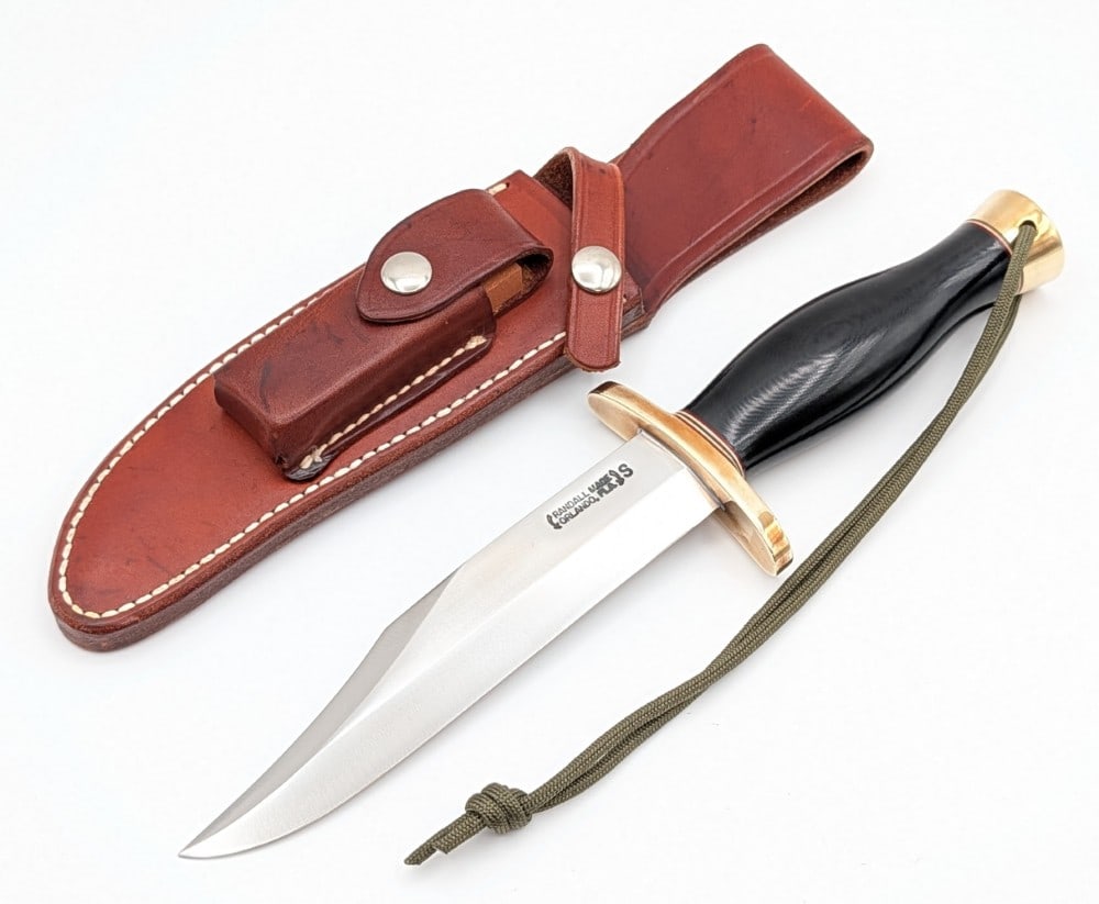 1980's Randall Model 12 6in Sportsman Bowie w/ Sheath: Features a stainless steel blade, a brass double upturned oblong guard, a black micarta commando handle, and a brass butt cap with a lanyard hole. Knife is in very nice condition with light scuffs and
