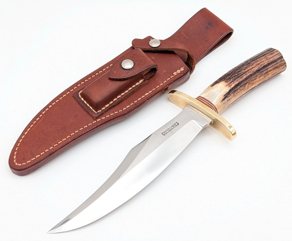 1980's Randall Model 12 8in Stag Bear Bowie w/ Sheath: Features a semi mirror polished bladed, a brass double upturned oblong guard, a stag handle, and a brass butt plate. Knife is in nice cleaned condition with light scuffs and some pits on the polished 