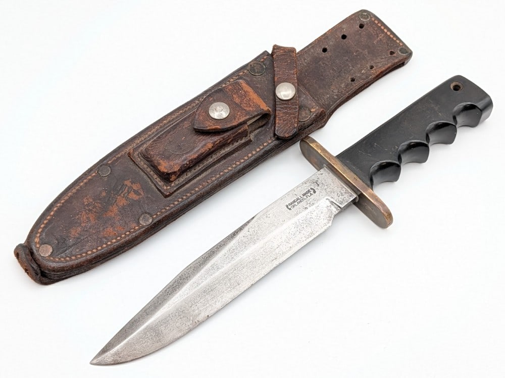 Vietnam Era USMC Randall Model 14 Attack Knife w/ Riveted Sheath: Features a named blade marked D. Blockley USMC 2060608, a brass double oblong guard, a full tang handle construction, and a micarta finger groove handle with a micarta lined lanyard hole. The sheath f