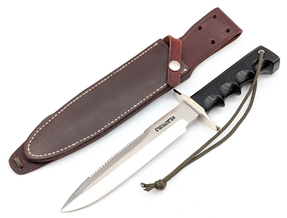 Randall Model 16 SP#1 Sawtooth Grind Special Fighter w/ Waxed Sheath: Features a stainless steel blade with a sawtooth grind, a nickel silver double downturned guard, a full tang handle construction, and a black micarta finger groove handle with a lanyard hole. Knife is