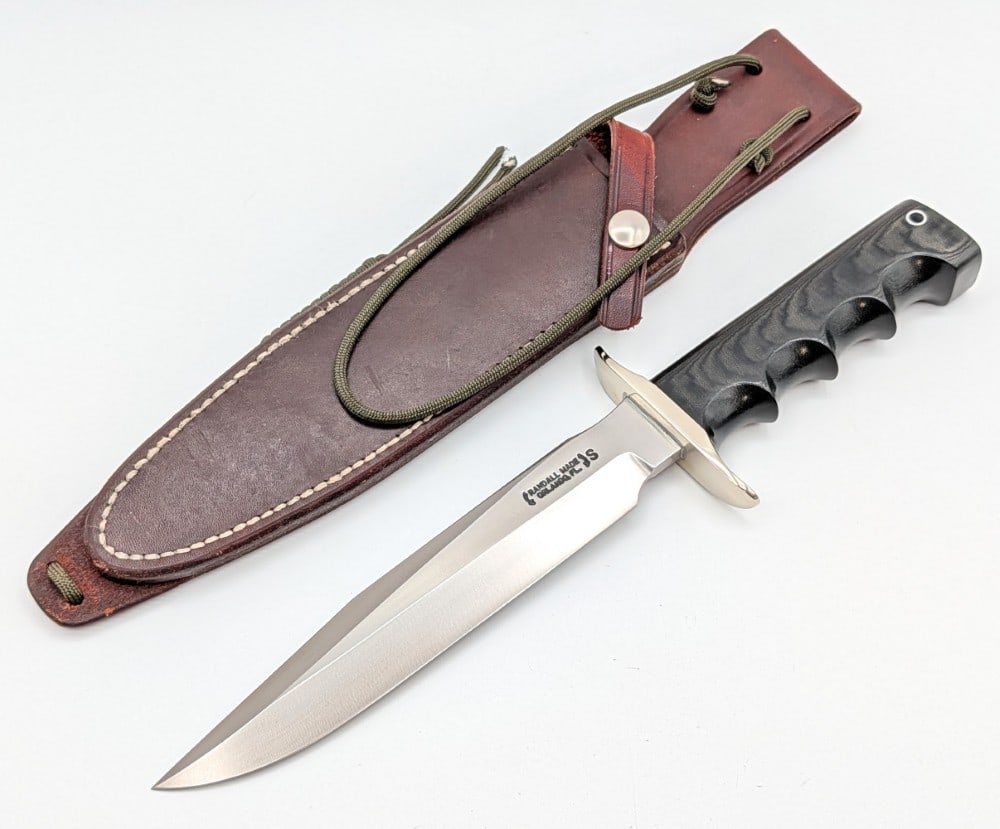 Randall Model 16 SP#1 Special Fighter w/ Waxed Sheath: Features a stainless steel blade, a nickel silver double downturned guard, a full tang handle construction, and a black micarta finger groove handle with a lanyard hole. Knife is in like new condition