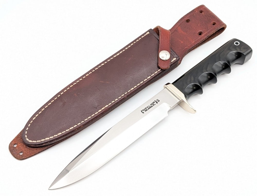 Randall Model 16 Diver Knife w/ Waxed Sheath: Features a stainless steel blade with thumb notches, a nickel silver single downturned guard, a full tang handle construction, and a black micarta finger groove handle with a lanyard hole. Knife is in