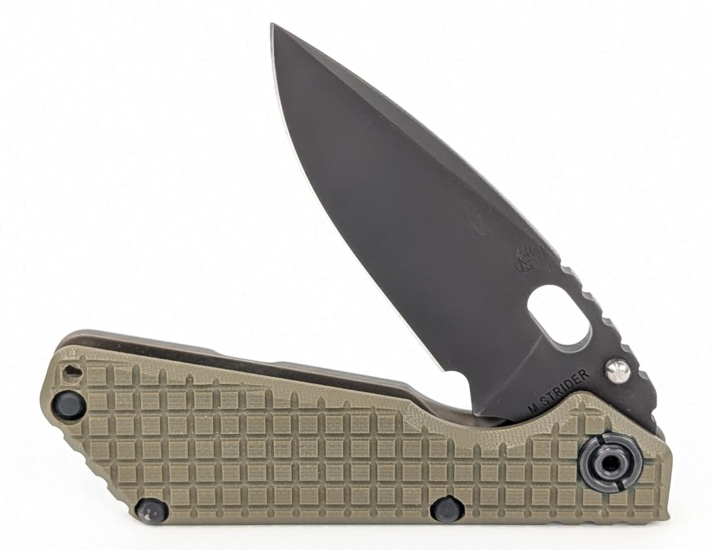 Mick Strider Knives Monkey Edge SnG Folding Knife: Features a black finish blade with a notched thumb rest, and a flame anodized titanium frame with a frag pattern green G-10 handle scale. Knife is in very nice condition with some light scuffs from ha