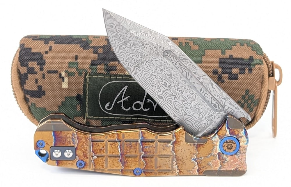 NIB 2025 Andre De Villers ADV Tracker Flipper Folding Knife w/ Carry Case: Features a damascus drop point fullered blade, a grenade grind acid rain etched titanium handle, blue anodized titanium accents, and a roller ball on the pocket clip. Knife is marked 03-2025. Knife is