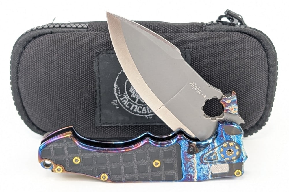 2022 Andre De Villers ADV Mini Alpha-s Button Lock Flipper w/ Carry Case: Features a gray finish drop point blade, an acid rain etched titanium handle with black G-10 inserts, and green anodized titanium accents. Knife is in like new condition. Overall measures 4-1/2in