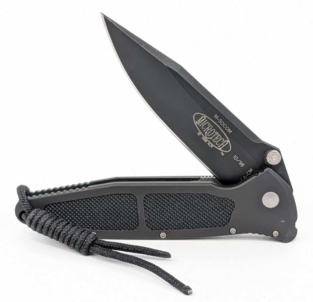 1998 Microtech Mini Socom Folding Knife: Features a black finish drop point blade, and an aluminum frame with rubber inserts. Knife is in very nice condition with some light scuffs and finish wear from handling. Overall measures 4in when