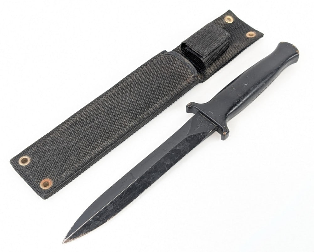 Gerber Guardian II Fighting Knife w/ Sheath: Features a black finish double edge blade with serial number A1380T, and a one piece guard and handle with a fused armorhide coating. Knife is in used condition with scratches and tarnishing on the bl