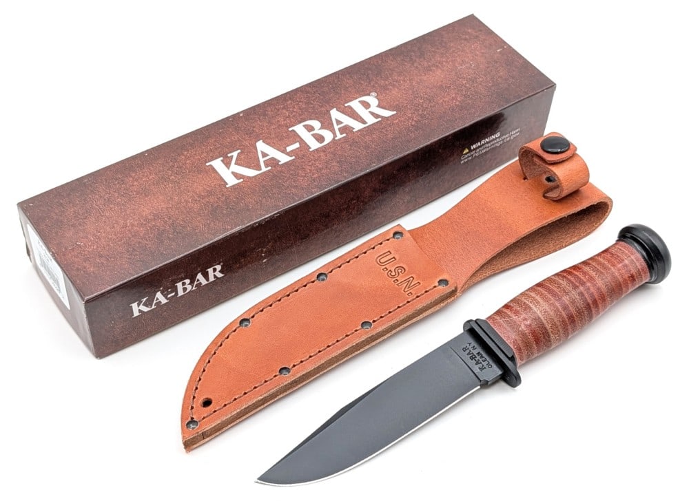 NIB Ka-Bar USN Mark I Fighting Knife w/ Sheath: Features a black finish blade, a black finish steel guard and pommel, and a stacked leather handle. Knife is in new condition. Blade length measures 5-1/8in and overall 9-1/2in.