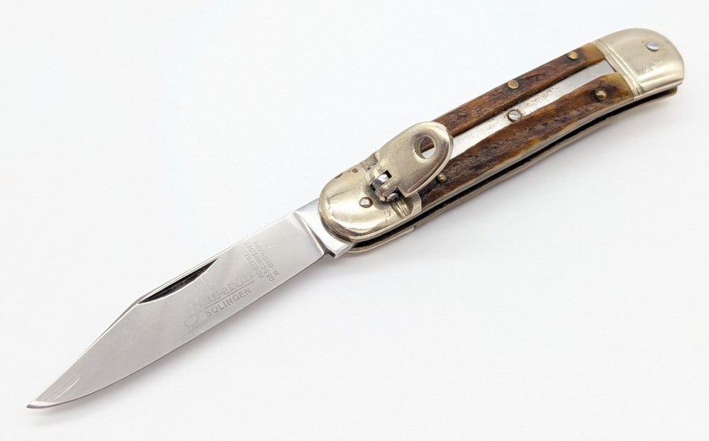 Hubertus Solingen Stag Leverlock Switchblade Knife: Knife is in fair condition with light scratches on the blade, scratches and dings on the bolsters, and the spring release is not working. Overall measures 3-1/2in when closed.