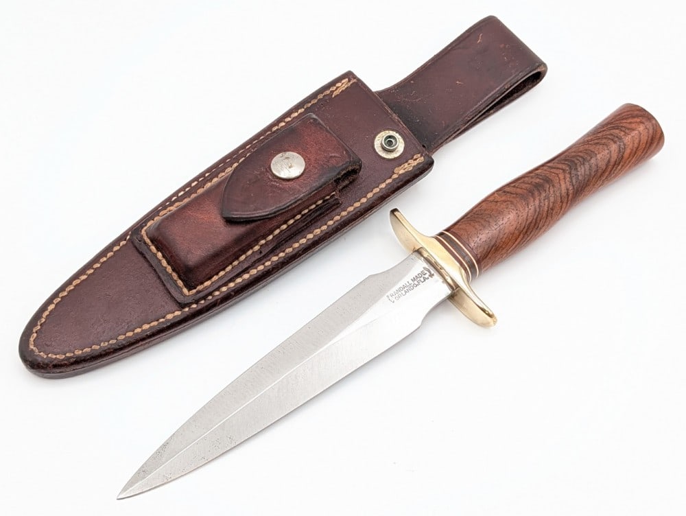 1970's Randall Model 2 6in Fine Walnut Stiletto Fighter: Features a brass double downturned guard, and a fine grained walnut handle. The sheath is missing the stone and the retaining strap. Knife is in good used condition with scratches on the blade, scuffs
