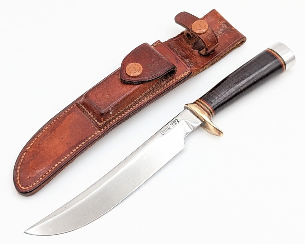 1950's Randall Model 3 7in Hunter w/ H.H. Heiser Sheath: Features a brass single downturned guard, a stacked leather handle, a duralumin butt cap, and a nut pommel. The sheath has nice brown buttons, is missing the stone, and a corn row back. Knife is in go