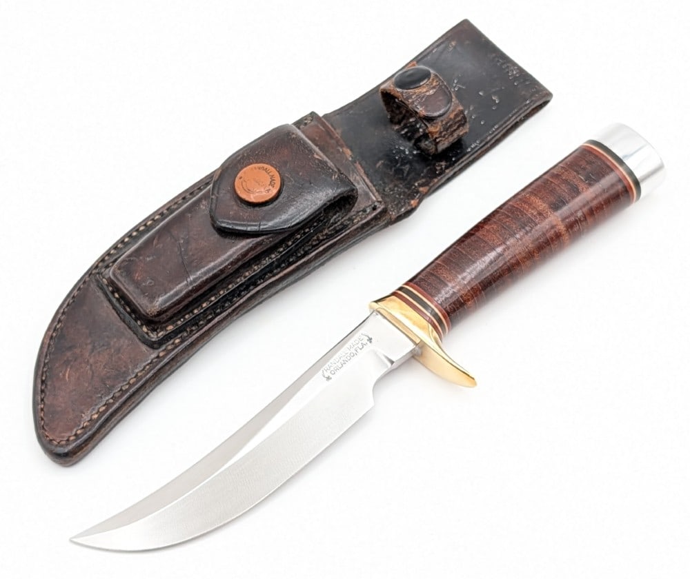 1950's Randall Model 4 5in Big Game Skinner w/ H.H. Heiser Sheath: Features a brass single downturned guard, a stacked leather handle, a duralumin butt cap, and a brass nut pommel. Sheath features a brown button stone snap, a black painted retaining snap, and a corn 