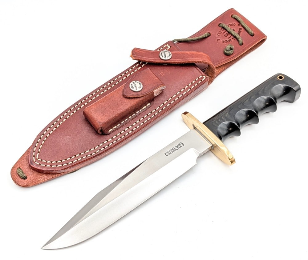 Randall Model 14 Black Micarta Attack Knife w/ Sheath: Features a brass double oblong guard, a full tang construction, and a black micarta finger groove handle with a lanyard hole. Knife is in very nice condition with some light scuffs and tarnishing on t