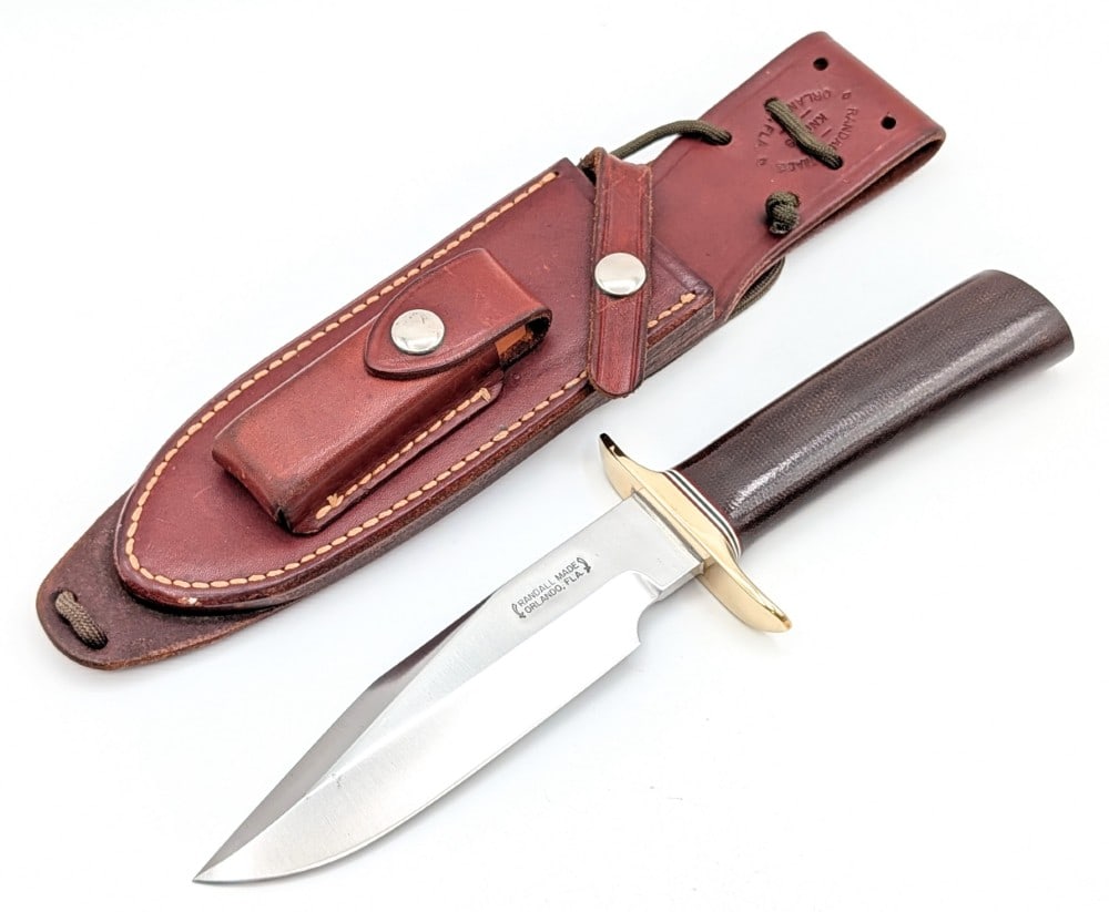1980's Randall Model 15 Black Micarta Airman w/ Sheath: Features a brass double downturned guard, and a standard black micarta handle. Knife is in nice condition with some small pit spots on the blade, and light scuffs and tarnishing on the guard. Blade le