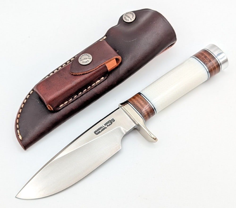 Randall Model 25 Ivorite Micarta Trapper w/ Sheath: Features a stainless steel blade with thumb notches, a nickel silver single downturned guard, an ivorite micarta handle with stacked leather spacers, and a duralumin butt cap. Knife is in very nice co