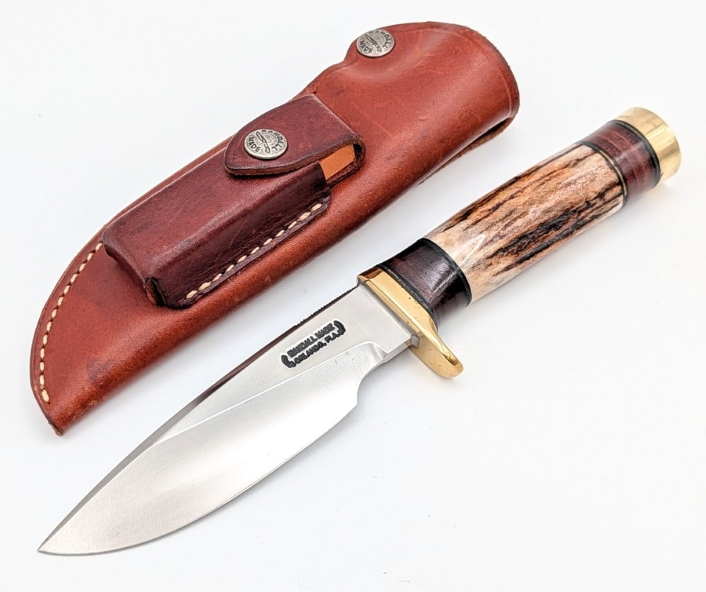 Randall Model 25 Stag Trapper w/ Sheath: Features thumb notches on the blade, a brass single downturned guard, a stag handle with stacked leather spacers, and a brass butt cap. Knife is in good condition with spots of tarnishing and some scr