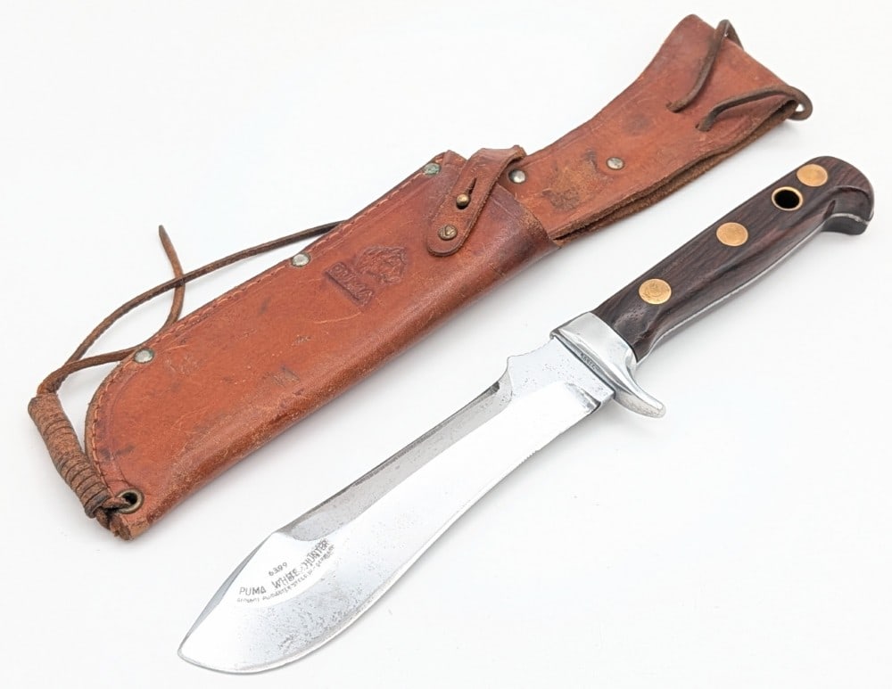1966 Puma Smooth Wood White Hunter 6399 w/ Sheath: Features a mirror polished blade with a sharpened spine and thumb notches, an aluminum guard with serial number 53606, full tang handle construction, and smooth wood handle scales with large brass pin