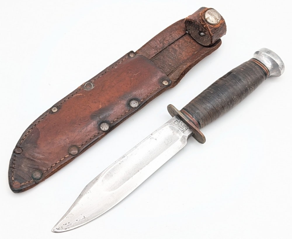 1940's-50's Marble's Ideal Hunter w/ Sheath: Features a fullered clip point blade with a right serif tang stamp, a brass double guard, a stacked leather handle, and an aluminum pommel with a small brass nut. Knife is in used aged condition with 