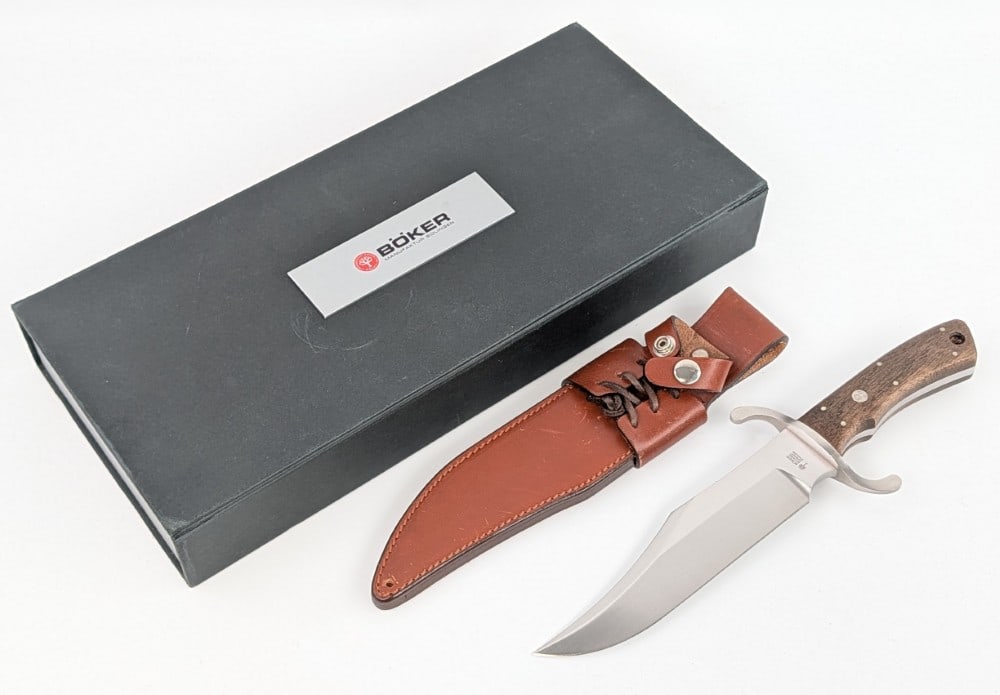 NIB Boker Solingen Smooth Wood Bowie Knife w/ Sheath: Features a satin finish clip point blade, a serpentine steel double guard, full tang handle, and smooth wood handle scales with a lanyard hole. Knife is in new condition. Blade length measures 7-3/4in