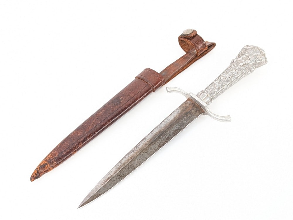 Cast Metal Hunting Scene Dagger w/ Sheath: Features a double edge blade, a serpentine double guard, and a cast metal handle with a hunting scene on either side. Knife is in aged condition with tarnishing on the blade, and scuffs and dings on t