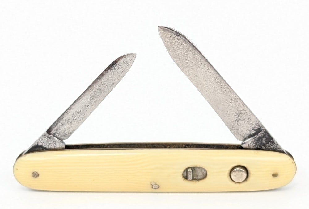 Schrade Cut Co. Synth White Double Switchblade Knife: Knife is in used condition with heavy scratches and pits on the blades, and light scuffs on the handle scales. Both blades have strong springs, but the main blade does not lock open. Overall measures 