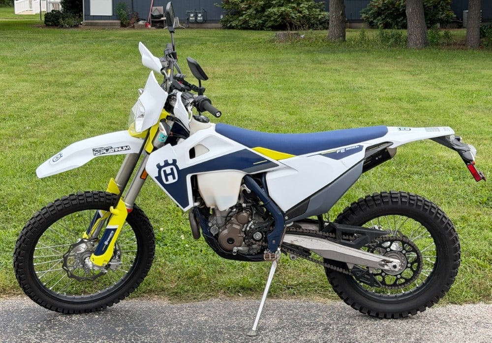 2021 Husqvarna FE 350s Dual-Sport Motorcycle: This is a Husqvarna FE 350s dual-sport motorcycle, featuring the brand's signature white, navy blue, and electric yellow color scheme. The machine is equipped with a street-legal package, including mi