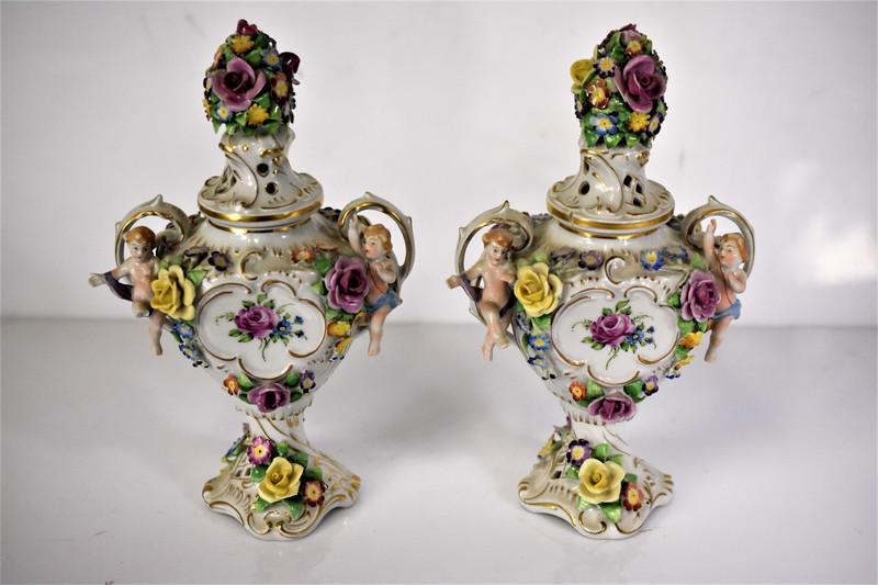 Von Schierholz German Porcelain Urn Grouping: Grouping includes (2) Von Schierholz porcelain urns with Figural Flowers and applied Angels and Flower Blossoms on Handles. In the manor of Dresden or Meissen. On (1) urn one of the Angel Legs has bro