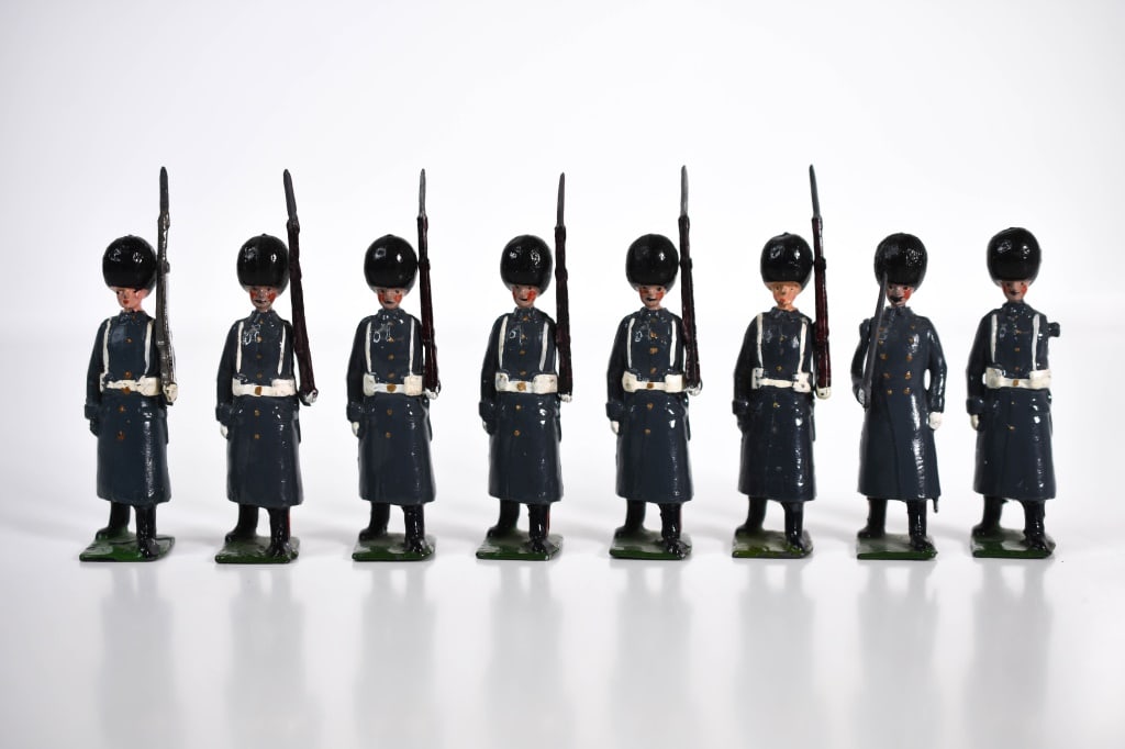 Britains Lead Grenadier Guards in Winter Dress: 7 guards. 1 is missing his arm. 1 officer. Movable arms. Roughly 2.25 inches tall. Some paint loss in areas.