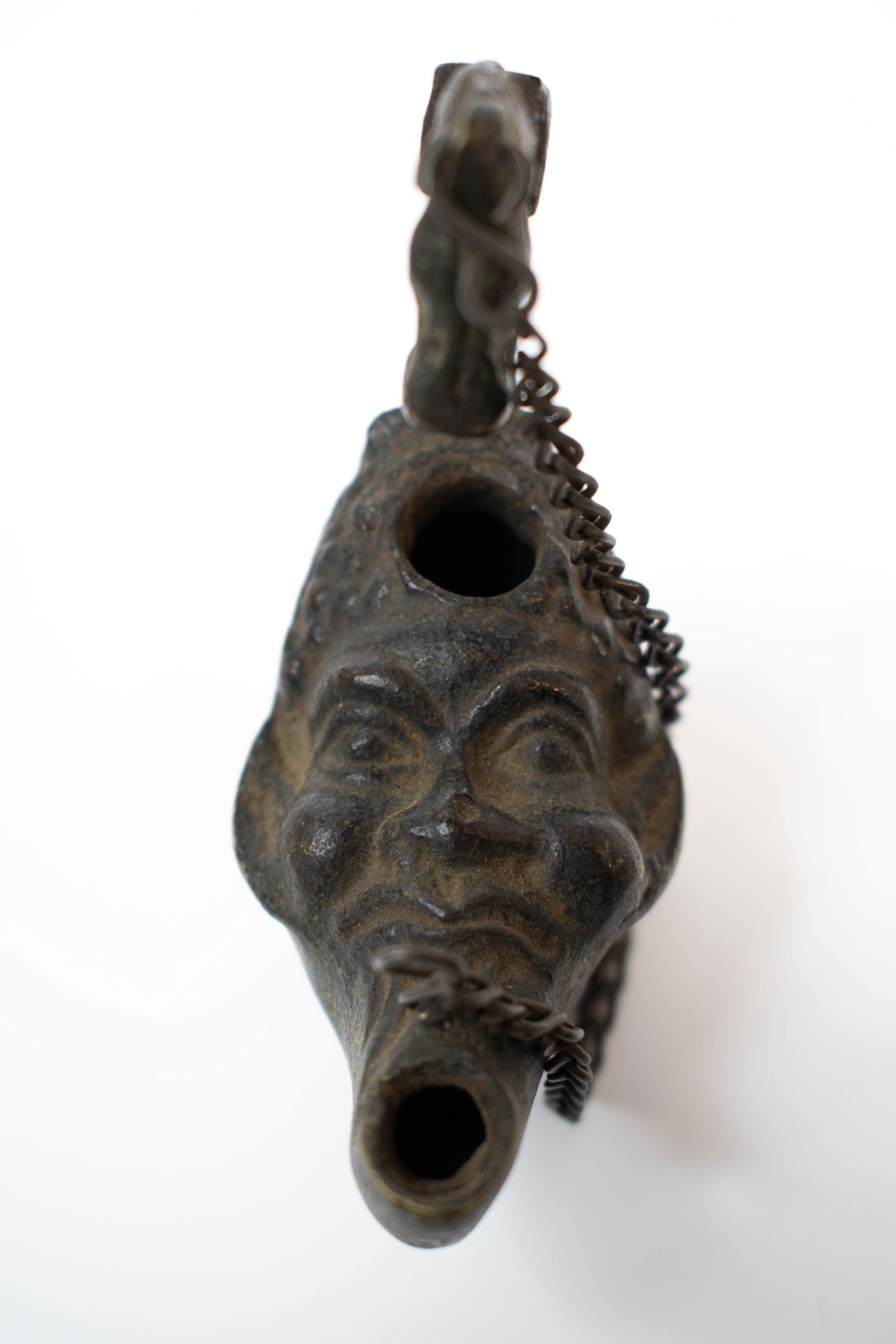 Ancient Roman Bronze Figural Oil Lamp: Antique Bronze Oil Lamp with Grotesque Mask and Horse-Head Handle A highly unusual cast bronze oil lamp featuring a whimsical grotesque face forming the spout and body, surmounted by a loop handle