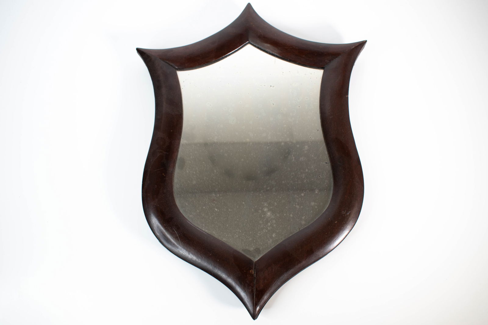 Antique Shield Form Wall Mirror: Antique Shield-Form Wall Mirror with Carved Wood FrameDistinctive antique wall mirror featuring a shield-shaped beveled wooden frame with a rich dark finish. The gently curved profile and hand-carved