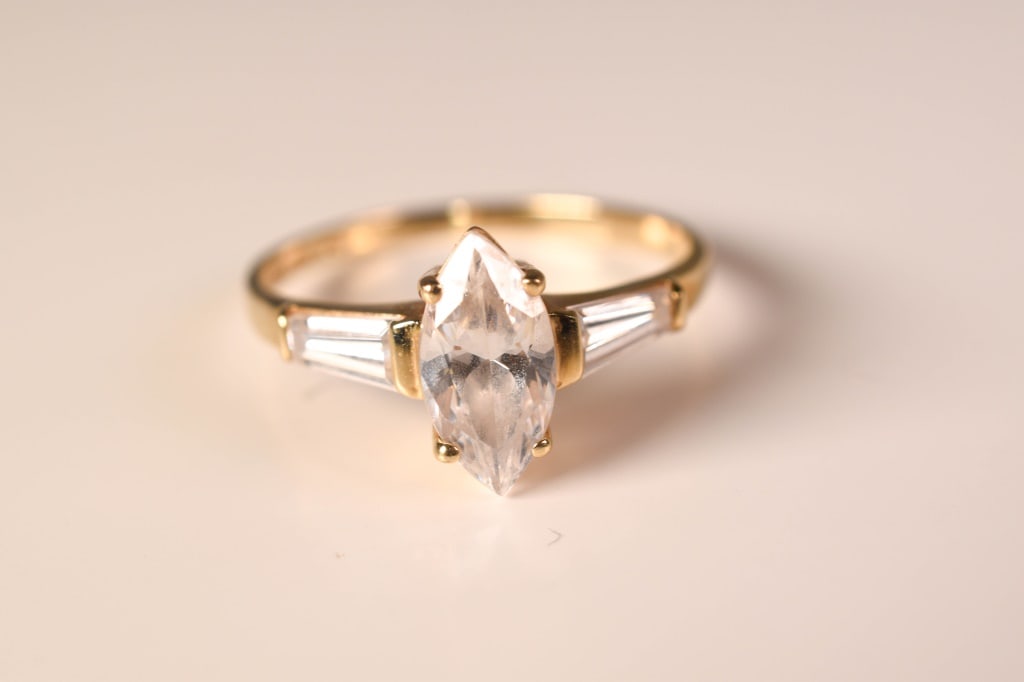 14K Gold & Marquise Diamond Simulant Ring 2.2 Gram: 3 diamond simulants: Apx 9.5mm x 4.5mm maruqise cut flanked by 2 baguette cuts Size: 6.75