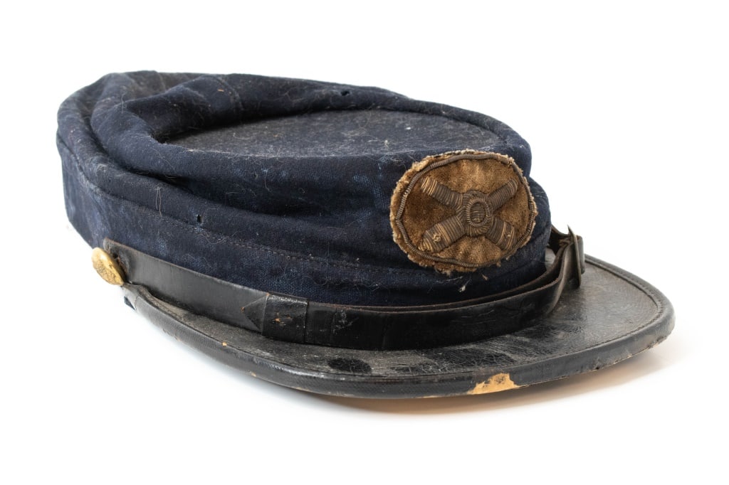US Army Artillery Kepi: Bullion artillery patch sewn on the front. Artillery A eagle buttons on the sides. Parts of a newspaper stuck to underneath the visor. Makers ink stamp is faint. Parts of the leather band are missing.