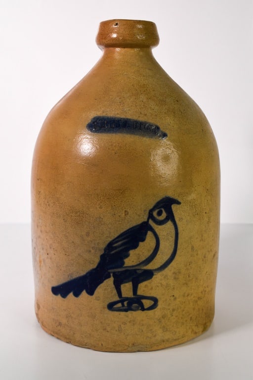 Whites Utica Blue Bird Decorated Stoneware Jug: Looks like a 1 gallon. Stamped Whites Utica. Some top rim roughness. Some chipping along the center of the jug. Mostly towards the backside. Bottom has multiple chips. Over 12 inches tall. Provenance: