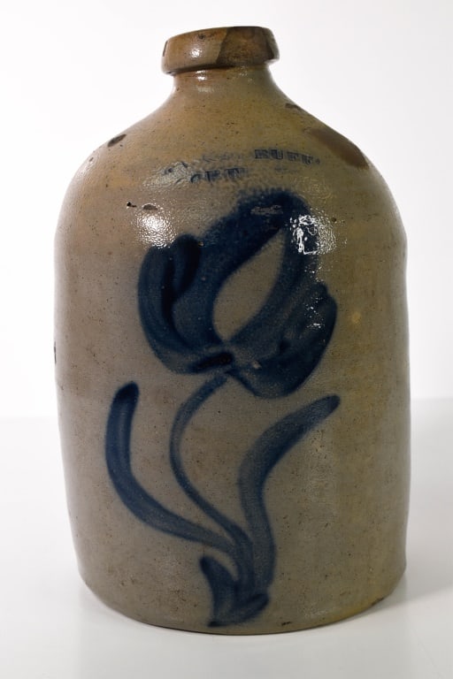 Woodruff Cortland Blue Decorated Stoneware Jug: Massive chip out of the top rim area. Faintly stamped Woodruff Cortland. Some discoloration in areas. Bottom looks good. Probably a 1 gallon. Under 12 inches tall. Provenance: Acquired from a single o