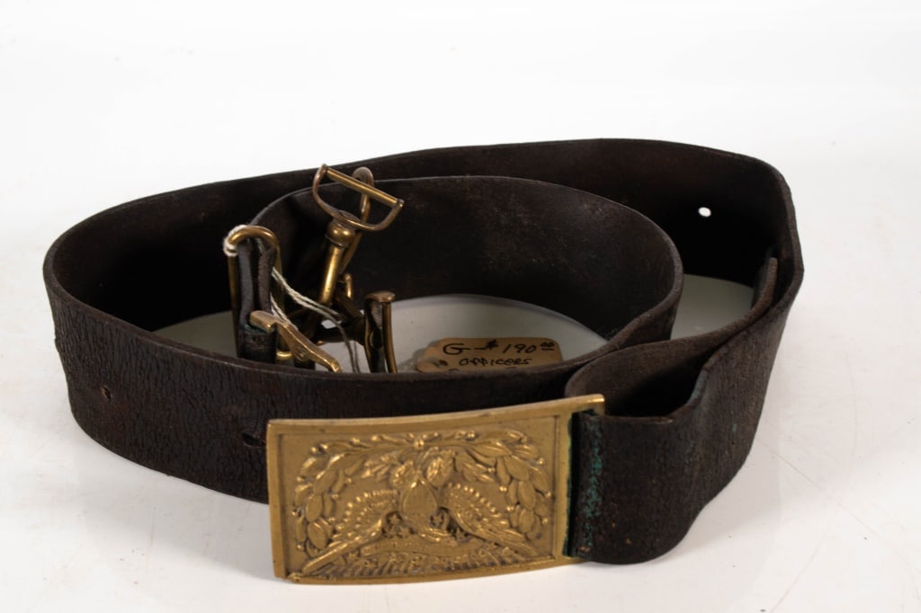 US Army Model 1874 Brass Belt Buckle: Brass keeper is numbered 263. Matching number on the buckle. Has sword hanger hookd. Leather belt is well worn. Length of belt is 33 inches. Provenance: Acquired from a single owner private estate col