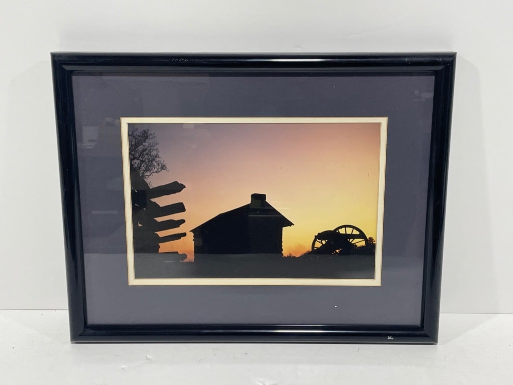 Photograph or Print of Barn: Photograph depicting a silhouette landscape at sunset, featuring a small structure, wagon wheel, and fence posts. Presented in a black wood frame with a double mat. Frame dimensions are 18 W x 14 H.