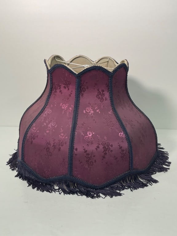 Antique Style Fabric Scalloped Lampshade: Purple fabric lampshade featuring a scalloped edge design. Decorated with floral patterns and bordered with ornate navy trim and fringe. The interior is lined and supported by a metal frame. Suitable