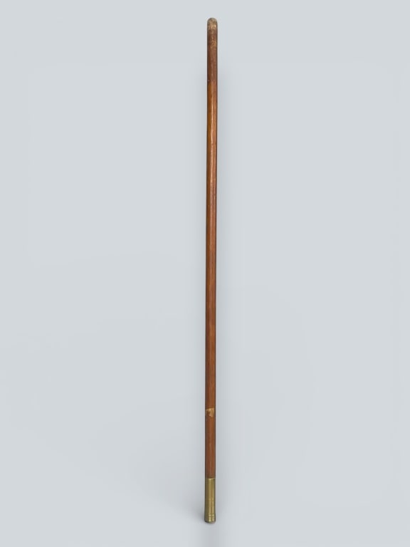 Walking Stick with Brass Tip: Straight wood cane featuring a smooth finish and a brass tip at one end. Measures approximately 43 H. The other end tapers into a rounded, unfinished tip. Provenance: Acquired from a single owner