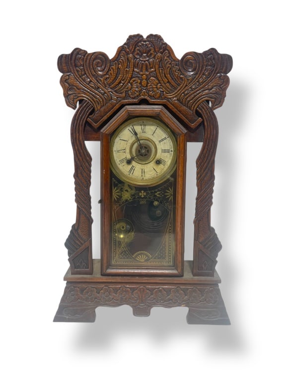 Antique Gingerbread Clock: Mantel clock crafted from carved wood with intricate detailing. Features a front-facing glass panel showcasing clockworks and etched decorative motifs. Roman numeral clock face with visible