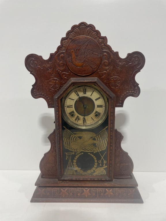 Antique Gingerbread Clock: Tall decorative wood clock featuring a carved crest with bird and floral motifs. Hexagonal clock face with Roman numerals and metal hands. Glass panel etched with an eagle and American flags.