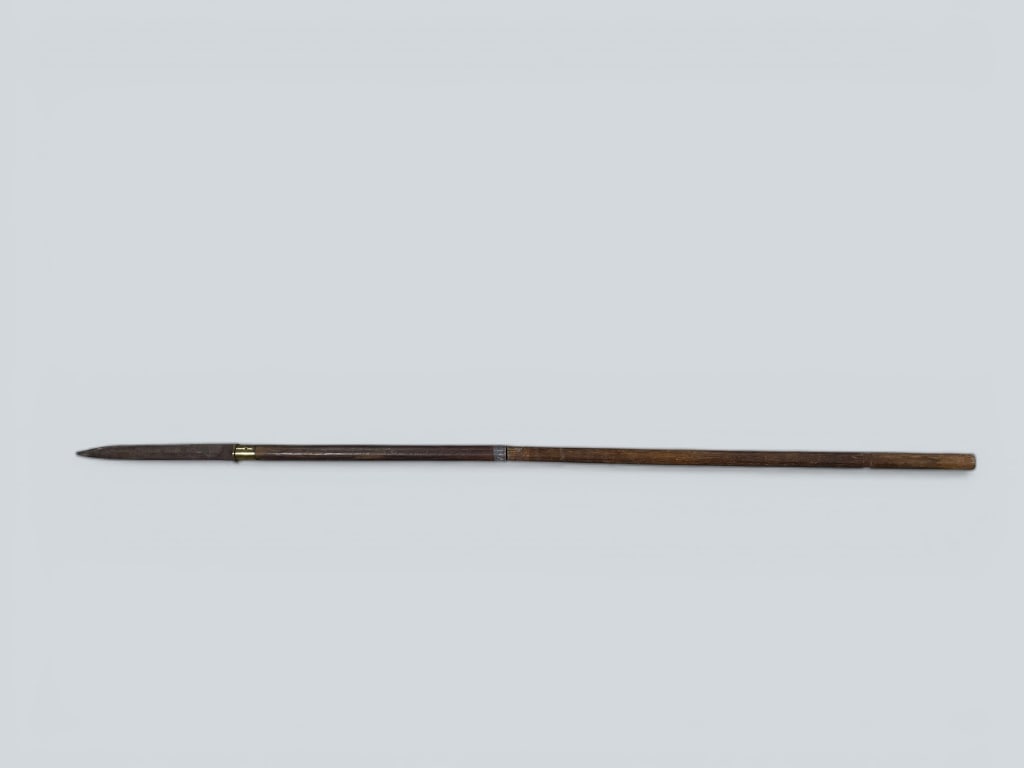 Esarly Wood and Metal Spear with Brass Accents: A wood and metal spear featuring a pointed metal blade and brass accents near the base of the blade. The spear measures 64 H. showcasing a natural finish on the wood and functional joinery along its l