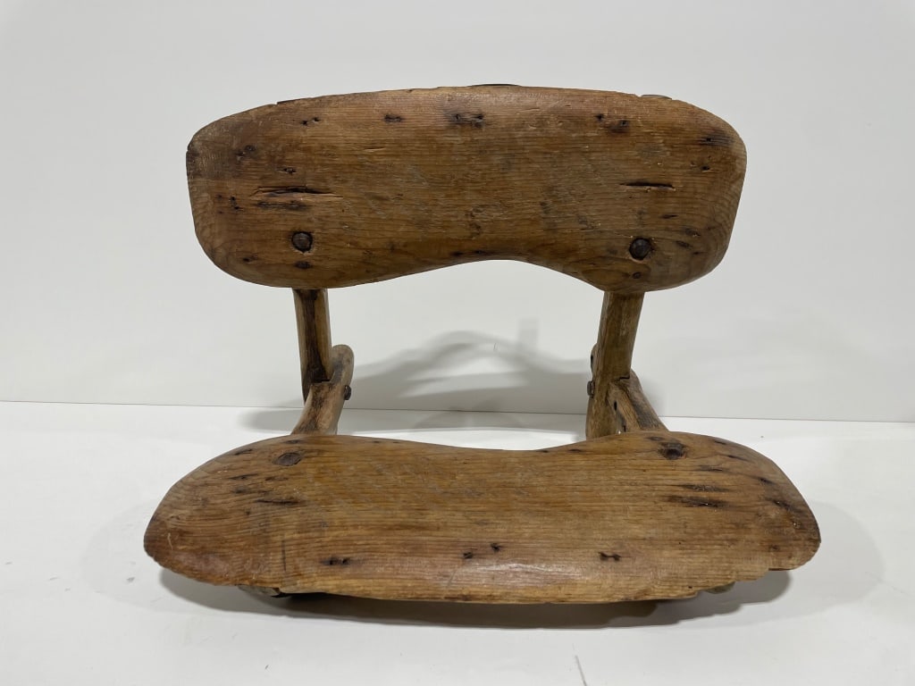 Early Folding Field Chair: Handcrafted wood toy sled featuring a curved seat and backrest. Includes a black strap with metal rings attached to the back. Measures approximately 20 W x 15 H. Exhibits a rustic design with natural